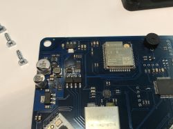Fragment niebieskiej płytki drukowanej z widocznym modułem ESP32, kondensatorami i innymi elementami elektronicznymi.