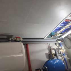 Instalacja hydrauliczna z białym bojlerem, niebieskim zbiornikiem i rurami.
