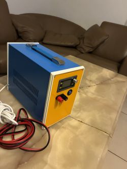 Blue bench power supply with a yellow front panel, display, knob and red/black terminals on a table by cables