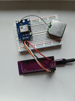 GPS module and prototyping board connected to a purple microcontroller board with wires.