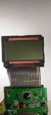 Image of a disassembled LCD display with a connected ribbon cable and printed circuit board in the background.