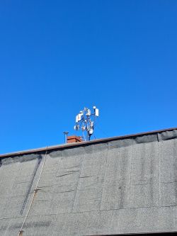 Zestaw anten na maszcie na dachu budynku na tle bezchmurnego, niebieskiego nieba