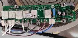 Green PCB with relays, capacitors, and connected wires, with a heating coil visible in the background