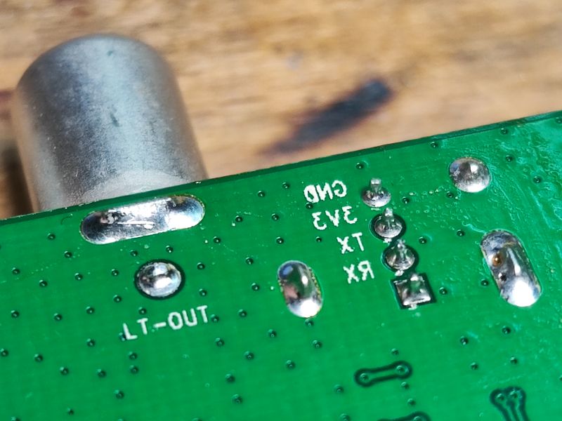 Zbliżenie na elementy elektroniczne dekodera telewizyjnego z oznaczeniem GND, 3V3, TX, RX na zielonej płytce PCB.