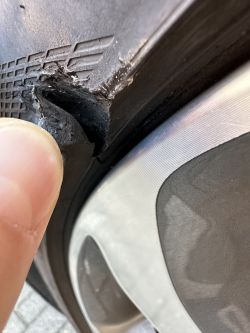 Zbliżenie na pęknięcie na oponie samochodowej, wskazywane przez palec.