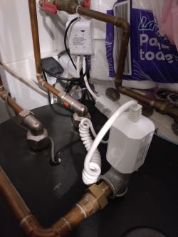 Copper pipes and valves on a tank, with a white Smart Plug controller and a coiled white cable