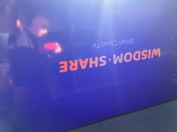 TV screen showing reflection of person and upside-down WISDOM SHARE text