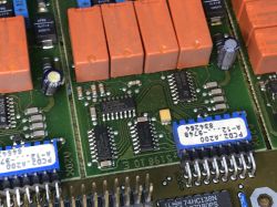 Close-up of a PCB with orange relays, IC chips, and blue DIP switches