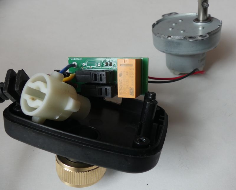 Electronics module with PCB, relay and wires, plus a separate electric motor on a light surface