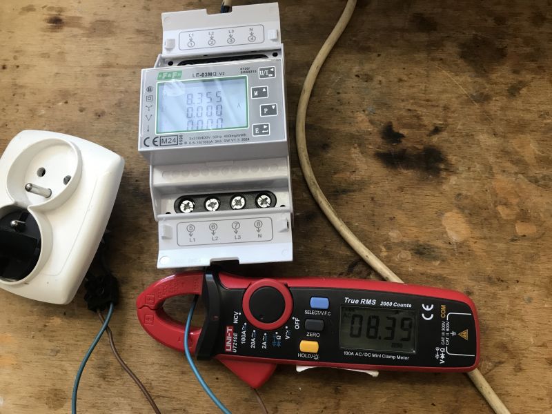 Jednofazowy licznik energii elektrycznej LE-03MQ podłączony do miernika cęgowego na drewnianym stole.