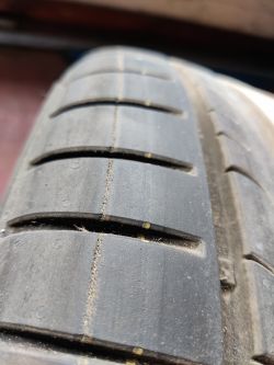 Zbliżenie na oponę Dunlop SP Sport Bluresponse z pęknięciami w pobliżu fabrycznych kolorowych pasków.