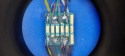 Zbliżenie płytki PCB z polami lutowniczymi i przylutowanymi przewodami na niebieskim tle