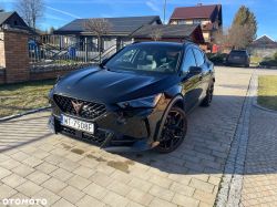 Black Cupra SUV parked on a paved driveway in front of houses.