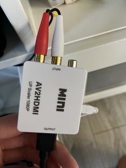 Przejściówka AV2HDMI trzymana w dłoni z podłączonymi kablami RCA i HDMI.