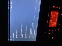 Ekran systemu multimedialnego z informacjami o urządzeniu, obok panel klimatyzacji.
