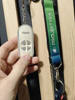 Zamel 4-channel remote held in hand against wooden slats background