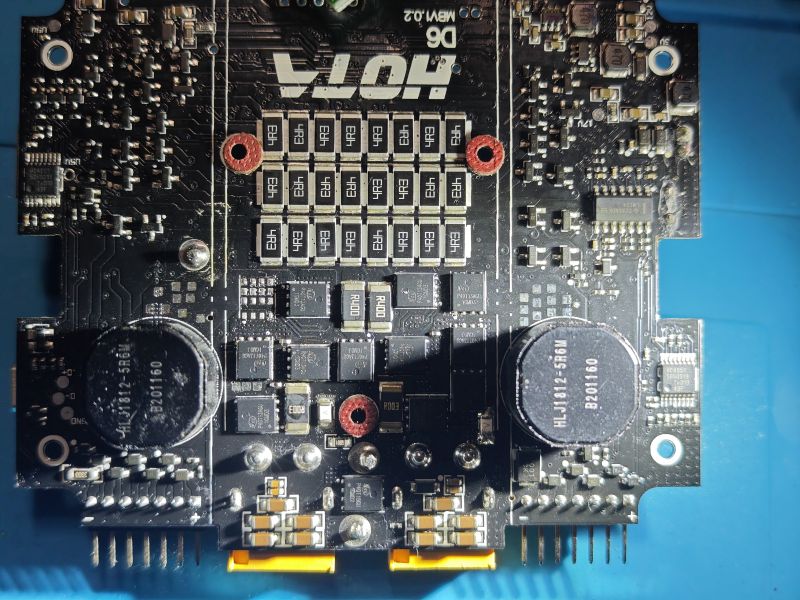 Płytka PCB z logo HOTA, dwa duże kondensatory i rzędy elementów SMD na niebieskim tle