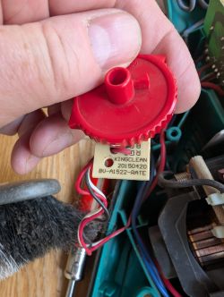Red Gear with KINGCLEAN Label inside an Electronic Device A red plastic gear with wires and a metal label held in a hand, with the interior of an electronic device in the background.