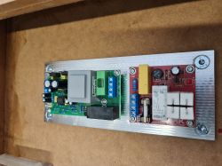 Zbliżenie na wewnętrzny moduł elektroniczny subwoofera, zamontowany na aluminiowej płycie.