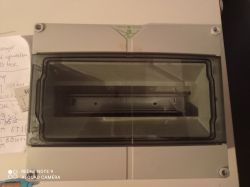 Szara rozdzielnica elektryczna z przezroczystą pokrywą, umieszczona na stole.