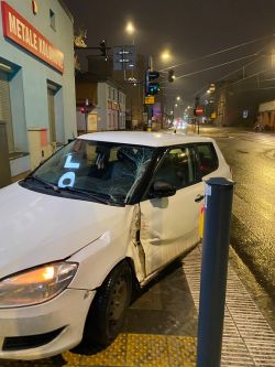 Uszkodzona Skoda Fabia po kolizji z tramwajem nocą w Łodzi Biała Skoda Fabia z uszkodzoną karoserią i pękniętą szybą po kolizji, nocą na skrzyżowaniu.