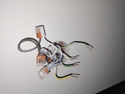 Kilka wystających przewodów elektrycznych z puszki w ścianie, część z nich podłączona do złączek.