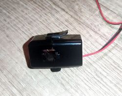 Black plastic sensor with a red wire on a wooden surface.
