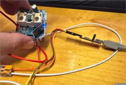 The image shows a hand holding an electronic board with connected wires in various colors, resting on a wooden surface.