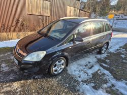 Black Opel minivan parked on a yard with patches of snow, next to a brown building