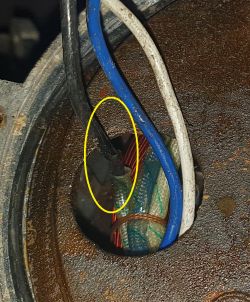 Zbliżenie na zardzewiałe połączenie elektryczne z kablami w różnych kolorach: czarnym, niebieskim i białym.