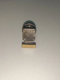 Small metal part with a flat gold contact connector on a light background