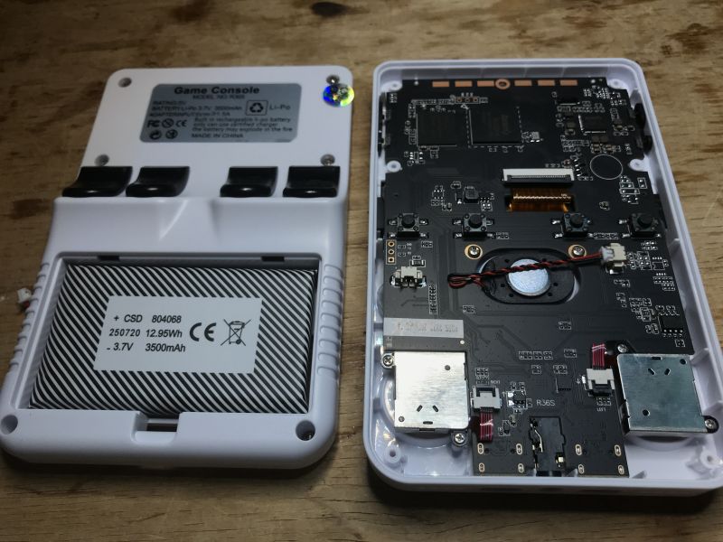 Opened R36S handheld console with visible battery and circuit board on wooden surface