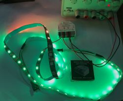 Green-lit LED strip connected to an ESP32 WLED controller on a desk, with the product box nearby.