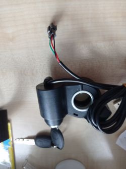 Stacyjka do hulajnogi elektrycznej z kablem i kluczykiem na stole.