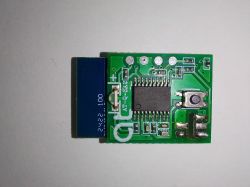 Close-up of an electronic PCB with push button Small green PCB with an IC chip, a push button, and a blue module on the left on a white surface