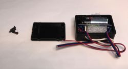 Opened plastic enclosure with AA battery, wires, and electronics inside, next to screws and a case cover.