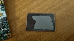 Uszkodzony wyświetlacz LCD z radiotelefonu Yaesu VX-2R na drewnianym blacie.