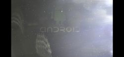 Słabo widoczny ekran z logo Androida w cieniu i refleksach świetlnych