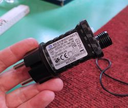 Zasilacz LED z etykietą techniczną trzymany w dłoni na tle czerwonej tkaniny