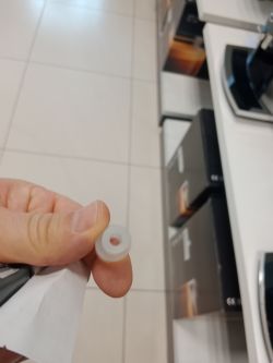 Osoba trzyma w palcach mały, przezroczysty, silikonowy element o cylindrycznym kształcie i otworze pośrodku.