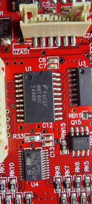 Zbliżenie na czerwoną płytkę drukowaną z widocznymi elementami elektronicznymi i chipami.