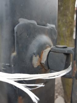 Zbliżenie na zawias bramy, z którego jedna śruba została wyrwana z metalowego słupka.