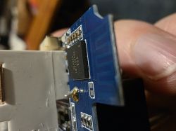 Close-up of a blue PCB with an integrated circuit and connector, held between fingers