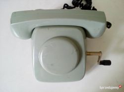 Stary telefon stacjonarny w kolorze jasnoszarym z korbką po prawej stronie.