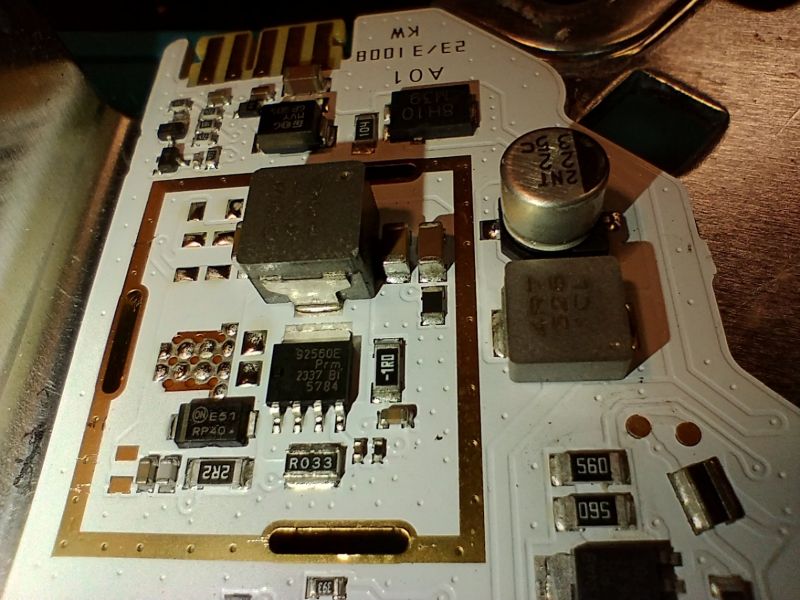 Zbliżenie na płytkę PCB z elementami elektronicznymi lampy LED samochodu, widoczne cewki, kondensator, układy scalone i ścieżki miedziane.