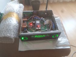 Open car radio case with circuit boards and a green display, on a table next to bubble wrap