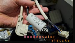 Ręka trzymająca przewody i kondensator z wtyczką 220 V oraz złączką.