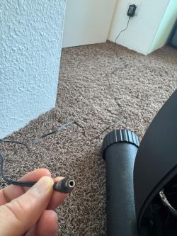 Stromstecker in Hand, Kabel verläuft über Teppich zu Netzteil an der Wand