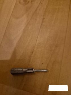 A screwdriver bit with an attached screw lying on a wooden surface.