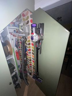 Cordless Dyson V8 vacuum cleaner hanging on a closet door with a floor head attached.